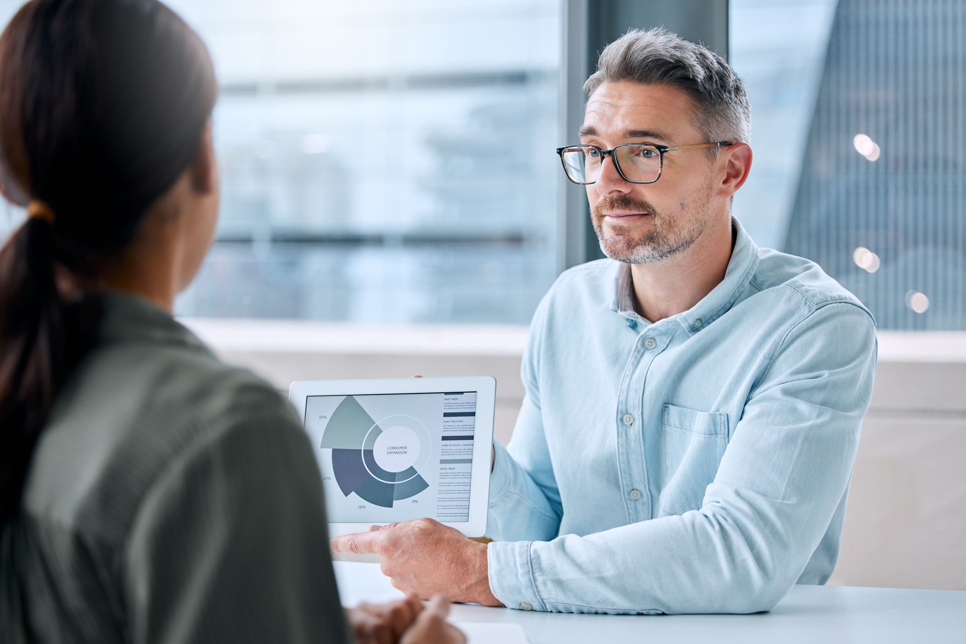 Shot of a mature businessman speaking to a colleague while analysing graphs on a digital tablet in an office Shot of a mature businessman speaking to a colleague while analysing graphs on a digital tablet in an office